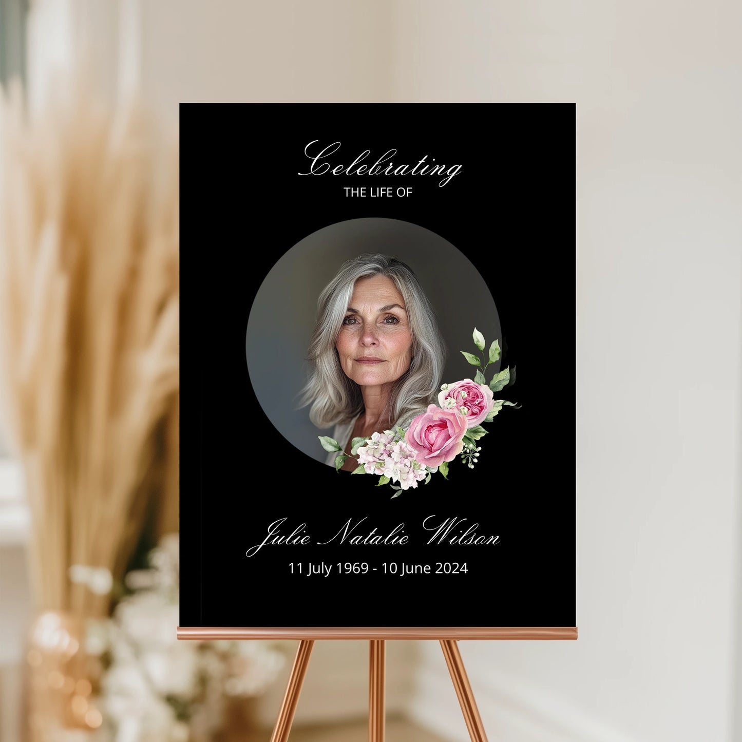 Memorial poster with a photo of a woman and floral design on a black background, displayed on an easel.