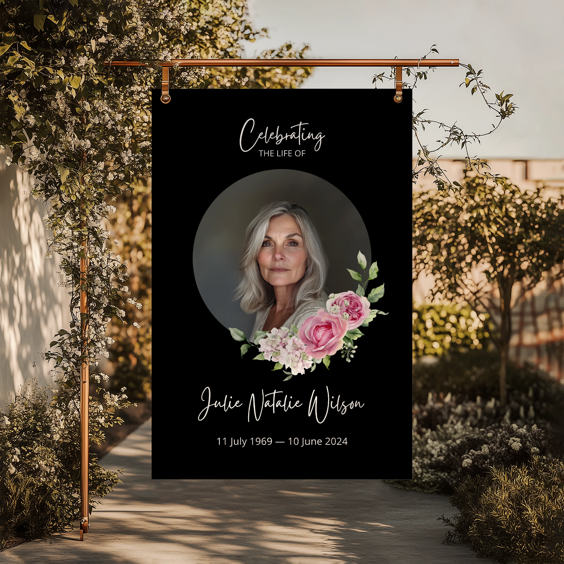 Memorial sign with a black background, featuring a circular portrait of a woman and pink floral accents. The text honours "Julie Natalie Wilson" with her birth and passing dates, serving as a beautiful tribute.