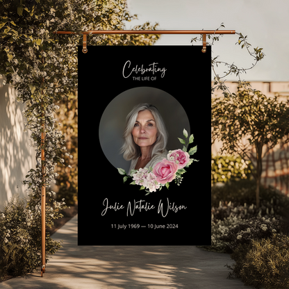 Memorial sign with a black background, featuring a circular portrait of a woman and pink floral accents. The text honours "Julie Natalie Wilson" with her birth and passing dates, serving as a beautiful tribute.