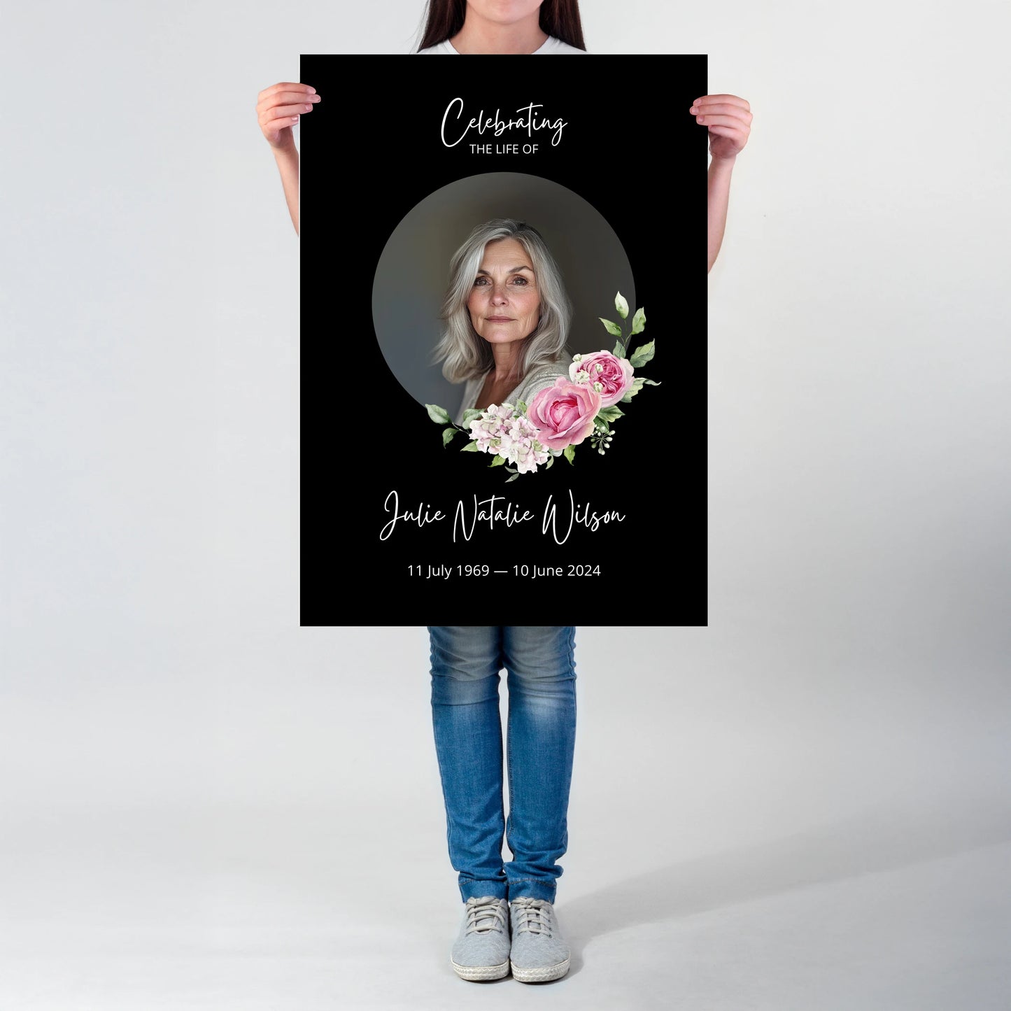 Memorial sign with a black background, featuring a circular portrait of a woman and pink floral accents. The text honours "Julie Natalie Wilson" with her birth and passing dates, serving as a beautiful tribute.
