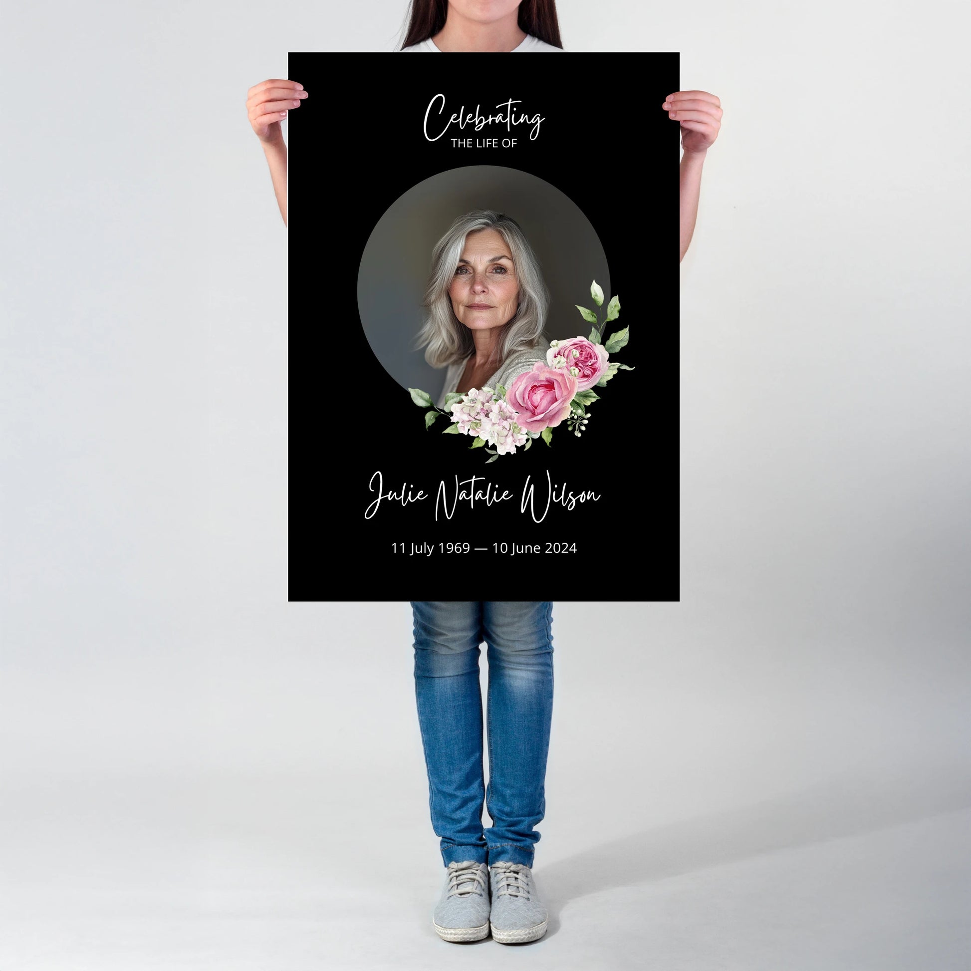 Memorial sign with a black background, featuring a circular portrait of a woman and pink floral accents. The text honours "Julie Natalie Wilson" with her birth and passing dates, serving as a beautiful tribute.