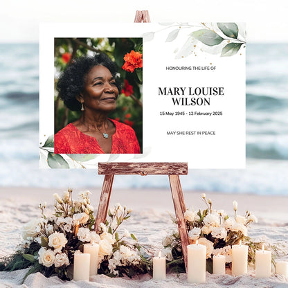 Memorial sign on a wooden easel at the beach, honouring a woman named Mary Louise Wilson. Features a soft eucalyptus design, her photo, name, and dates. Surrounded by white roses, candles, and flowers, creating a peaceful tribute.