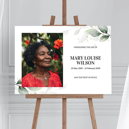 Memorial sign on a wooden easel at the beach, honouring a woman named Mary Louise Wilson. Features a soft eucalyptus design, her photo, name, and dates. Surrounded by white roses, candles, and flowers, creating a peaceful tribute.