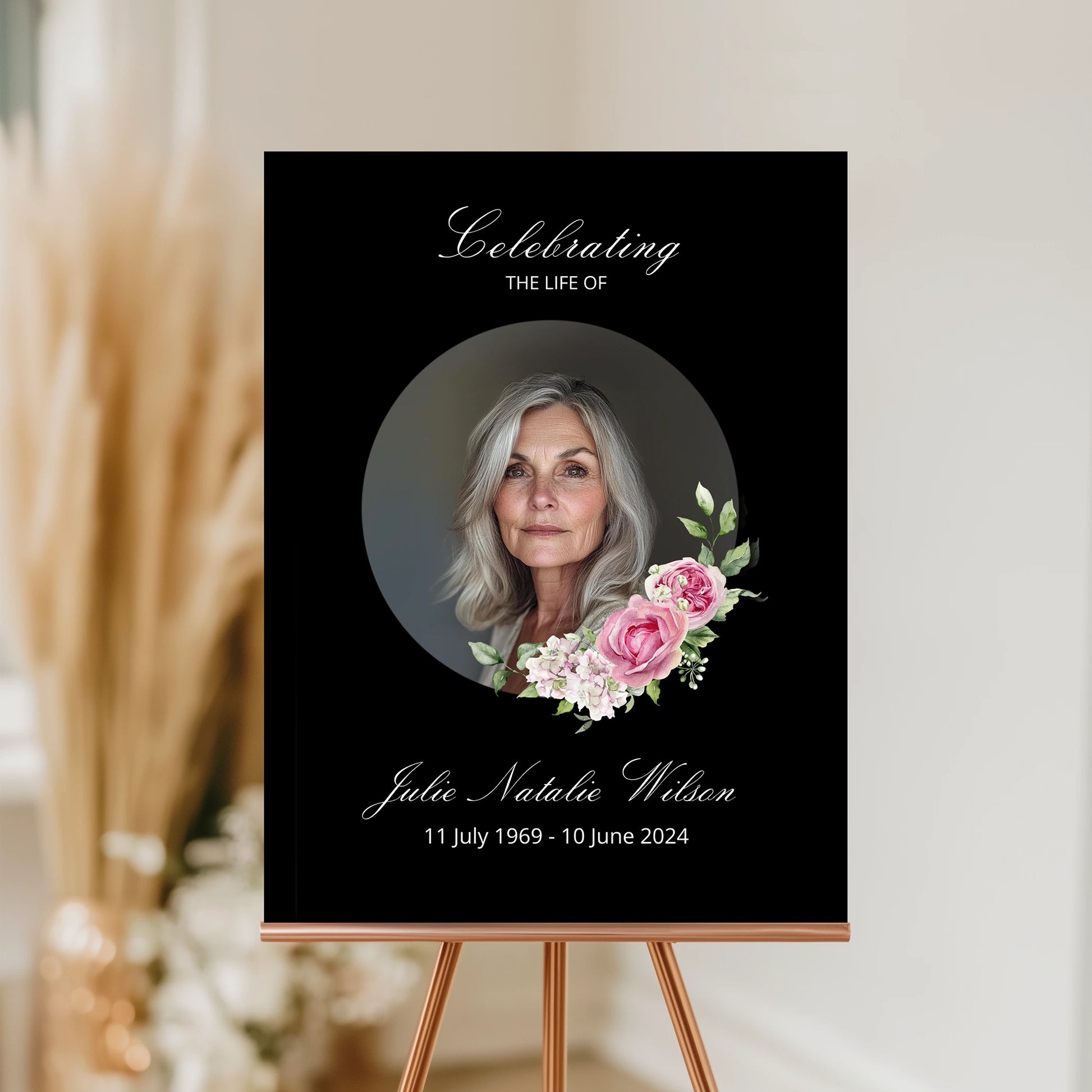 Memorial poster with a photo of a woman and floral design on a black background, displayed on an easel.